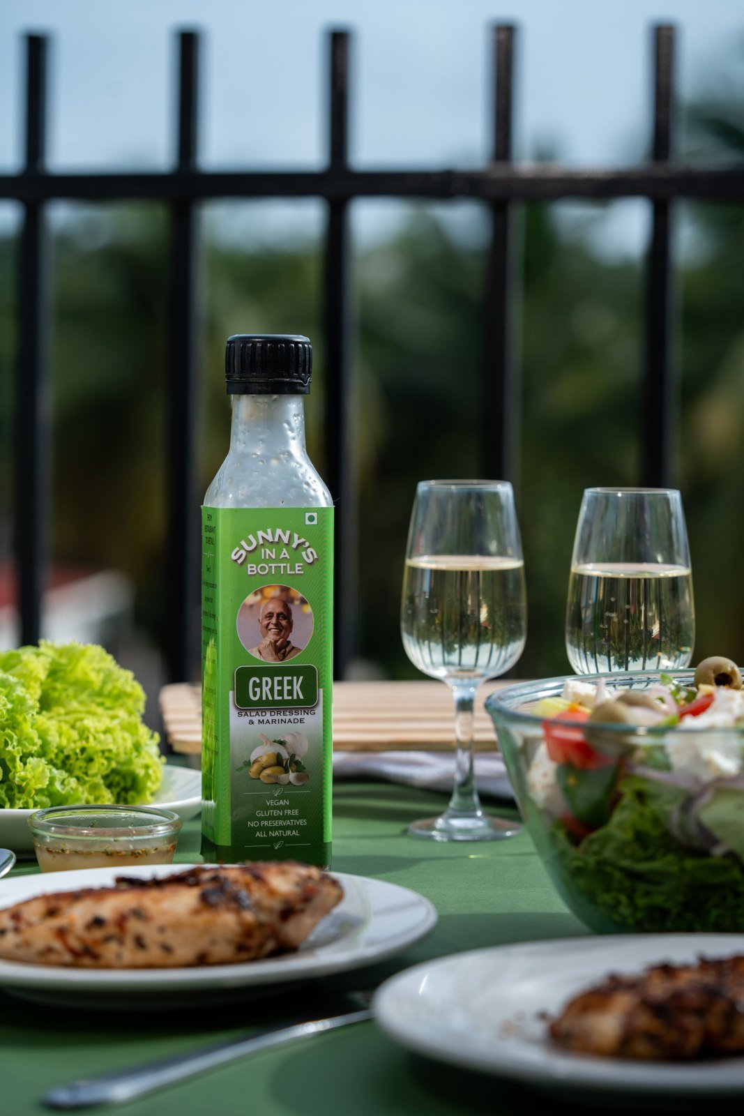 Sunny's In A Bottle Greek dressing on an outdoor dining table with grilled chicken and wine